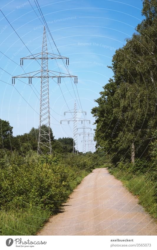 Überlandleitung und Hochspannungsmasten entlang Feldweg durch die Landschaft Hochspannungsleitung Strommast Natur Elektrizität ländlich Weg Straße