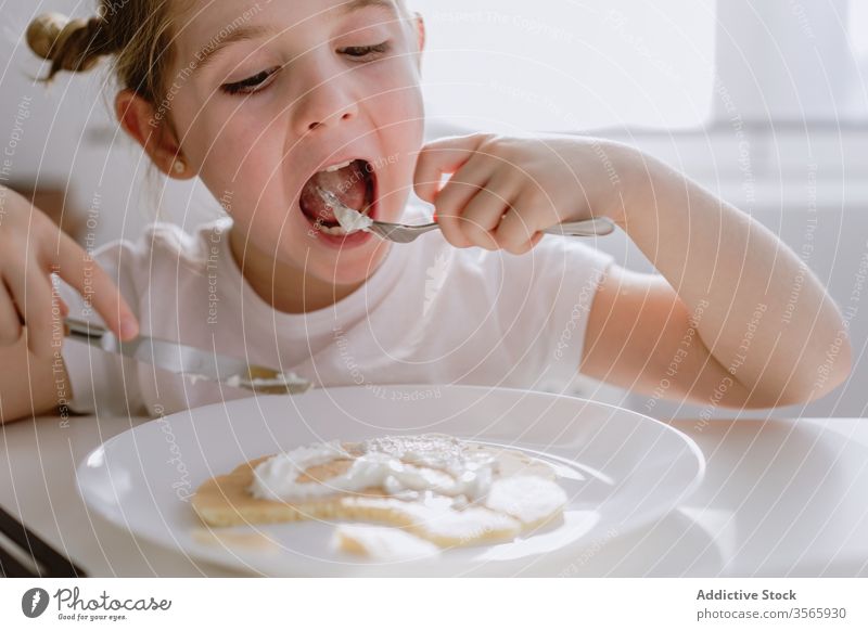 Aufgeregtes Mädchen frühstückt morgens in der Küche aufgeregt Kind Frühstück Pfannkuchen Nervenkitzel geschmackvoll gepeitscht Sahne Morgen bezaubernd lecker