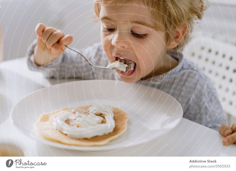 Kleines Kind isst Pfannkuchen mit Schlagsahne essen gepeitscht Sahne Küche bezaubernd lecker Frühstück hell Lebensmittel Tisch sitzen Kindheit geschmackvoll