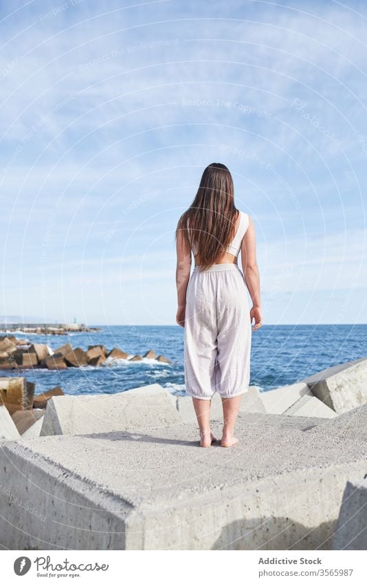 Anonyme moderne Frau, die auf dem Betonblock des Wellenbrechers steht MEER Harmonie Küste Zeitgenosse Konzept Stein Konstruktion Energie physisch jung Pose