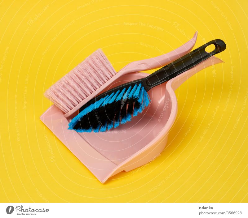 rosa Kunststoffschaufel und Reinigungsbürste auf gelbem Hintergrund Baggerlöffel schaufeln Single Atelier Kehren Bürste Arbeit Sauberkeit Raumpfleger Säuberung