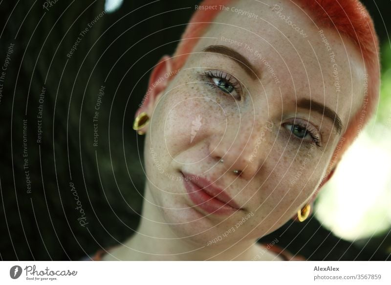Portrait einer jungen Frau vor einem Baum 18-25 Jahre schön Schlank Sommersprossen rothaarig schmuck Piercing Tätowierung Gesicht hellhäutig kurzhaarig weiß