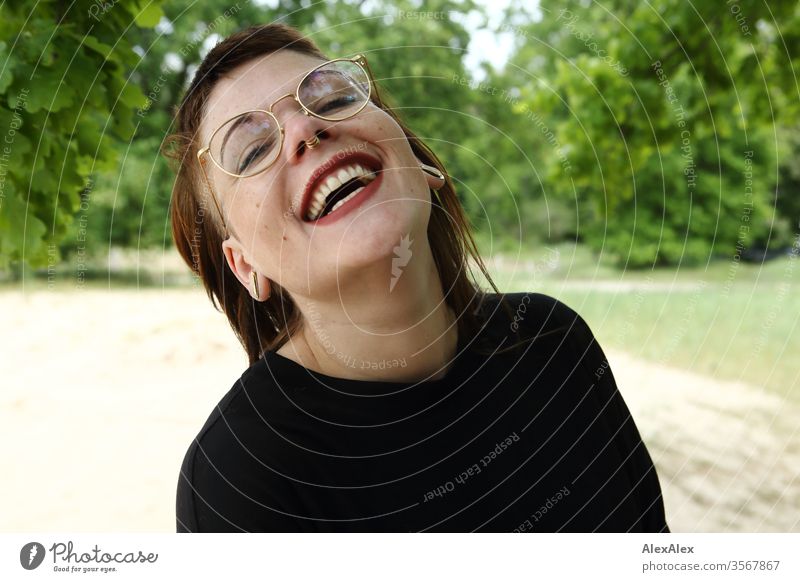 Portrait einer lachenden jungen Frau im Park Jugendliche schön stark alternativ groß Piercing Haut intensiv Blick schauen beaobachten stehen schlank ästhetisch