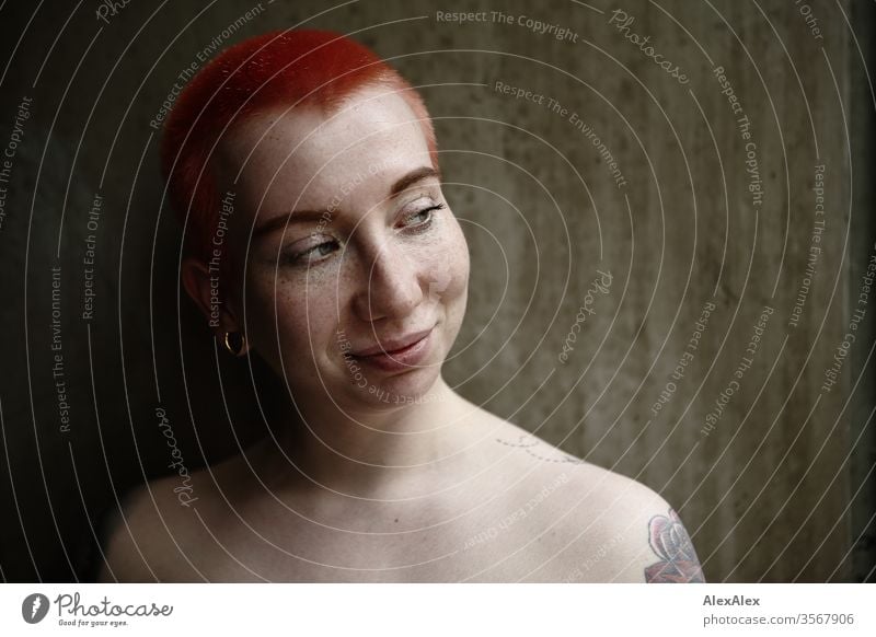 Portrait einer lachenden jungen Frau vor einer Betonwand 18-25 Jahre schön Schlank Sommersprossen Wand rothaarig schmuck Piercing Tätowierung Dekolleté Gesicht