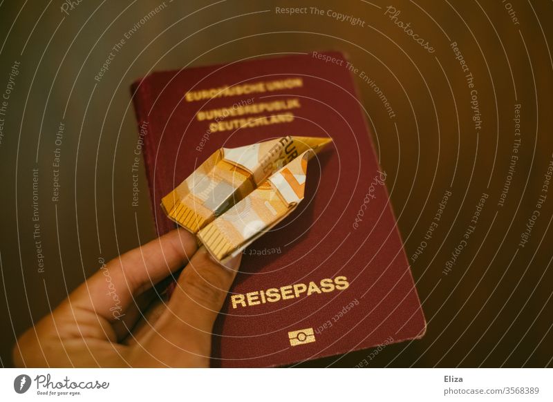 Eine Hand hält einen aus einem Geldschein gefalteten Papierflieger über einen deutschen Reisepass verreisen Reisekasse Urlaub Kosten Urlaubskasse fliegen teuer