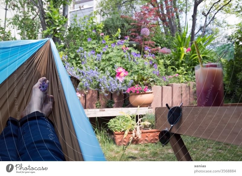 Füße in einer Hängematte mit Blick auf den Garten und bereitgestellten Drink - Tiefenentspannung garantiert Entspannung Erholung Sonnenbrille Getränk Saft Glas