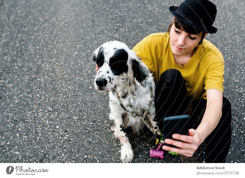 Junge Dame benutzt Smartphone, während sie mit Hund am Boden sitzt Frau Spaziergang Selfie Spaß Park Natur Hipster Subkultur Stil Zusammensein Begleiter Straße