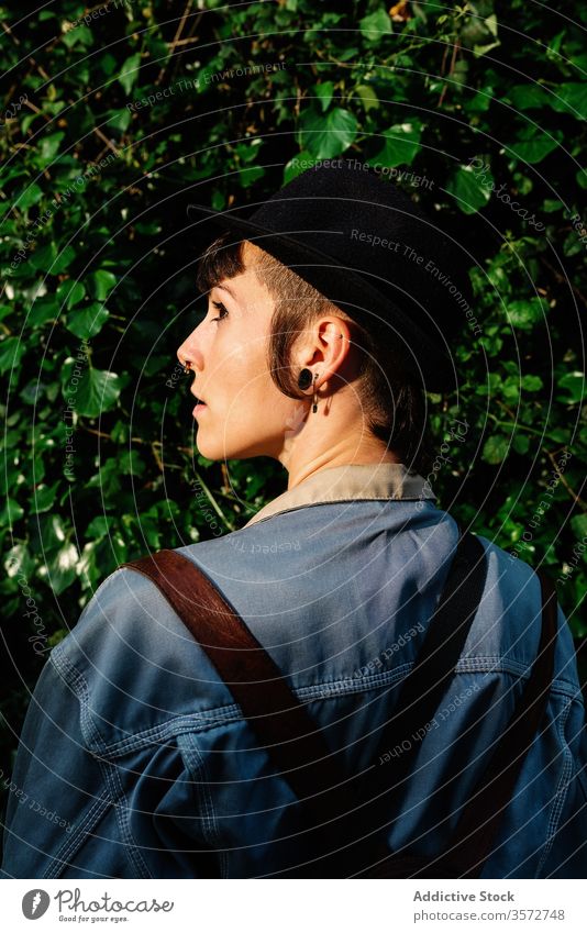 Stilvolle junge Dame mit Hut steht neben blühendem Busch auf der Straße Frau Rückansicht positiv Hipster Buchse Natur Subkultur charmant Menschliches Gesicht