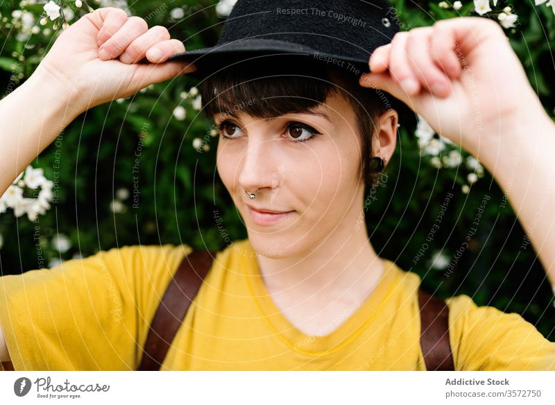 Stilvolle junge Dame mit Hut steht neben blühendem Busch auf der Straße Frau positiv Hipster Buchse Natur Subkultur charmant Menschliches Gesicht Porträt