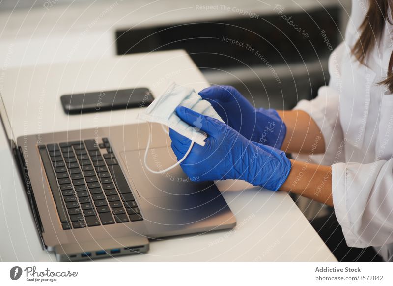 Frau mit Schutzmaske und Handschuhen am Laptop Coronavirus Mundschutz heimwärts Arbeit behüten benutzend abgelegen Arbeitsplatz Apparatur Gerät Sicherheit COVID