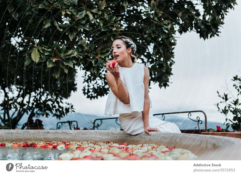 Junge Braut isst Apfel vom Brunnen Frau Springbrunnen Garten elegant jung frisch Hochzeit Biss Model Frucht Wasser nass Schalen & Schüsseln Sommer Park Stil
