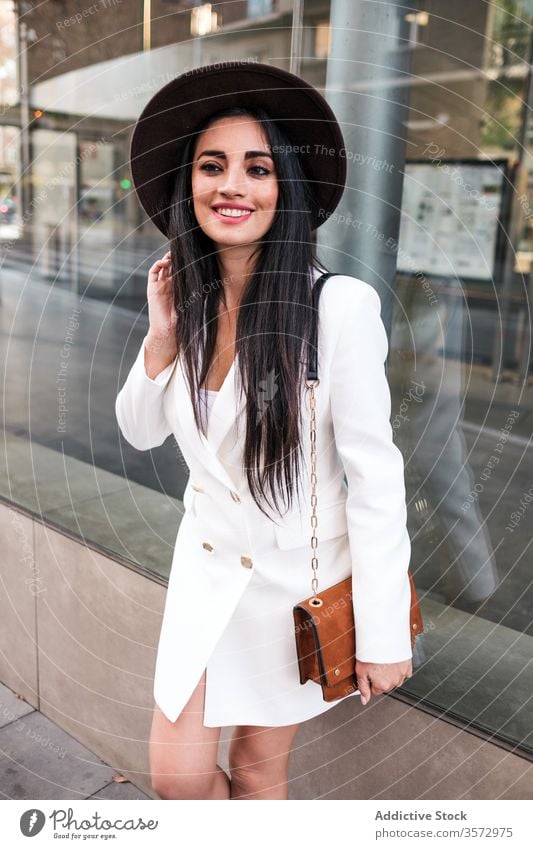 Modische junge Frau steht auf Stadtstraße Stil trendy Mode Großstadt Straße Frühling Hut Handtasche Saison Mantel positiv modern selbstbewusst Gebäude Glas