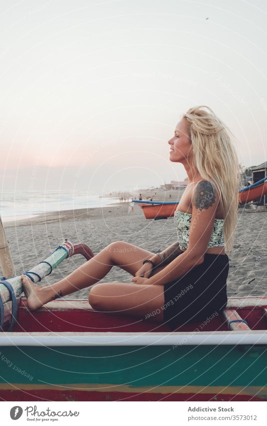 Fröhliche Dame ruht sich auf Holzboot am Sandstrand aus Frau Meer Küste Strand Sonnenuntergang Ufer Windstille Harmonie Einsamkeit Frieden Wasser Bank ruhen