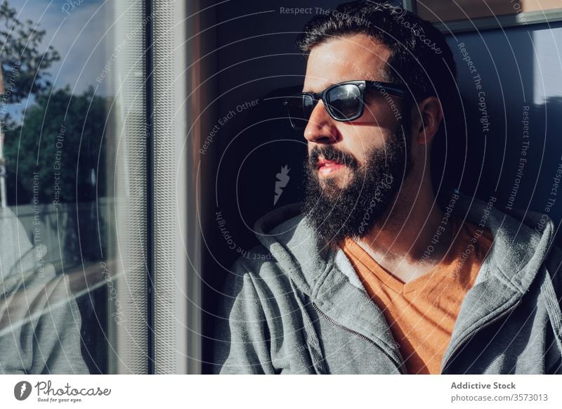 Nachdenklicher junger bärtiger Mann schaut durchs Fenster, während er mit dem Zug reist Ausflug reisen träumen besinnlich Sonnenlicht Sommer ernst Verkehr