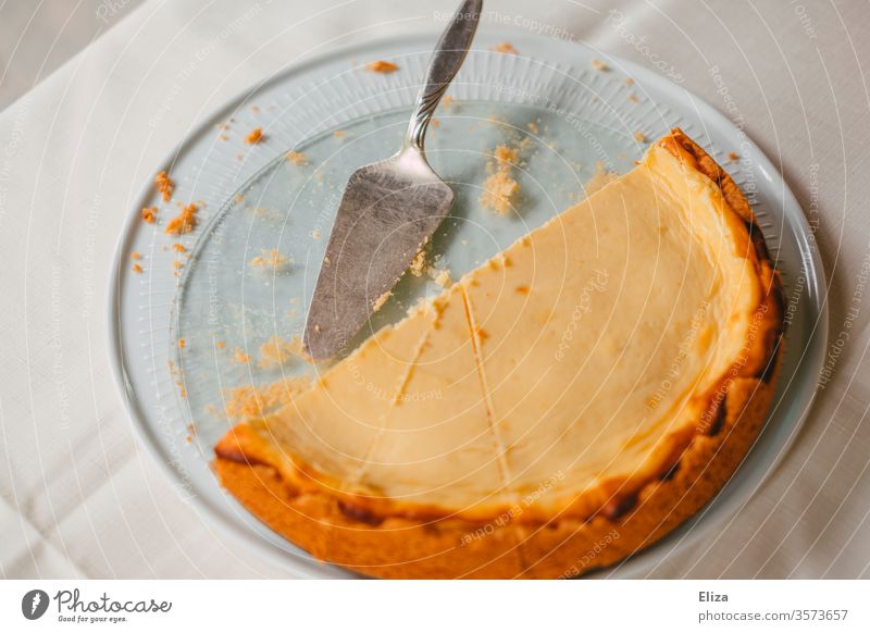 Eine Kuchenplatte mit einem halben Käsekuchen darauf essen lecker backen gebacken Tisch Kuchenheber süß Hälfte Krümel