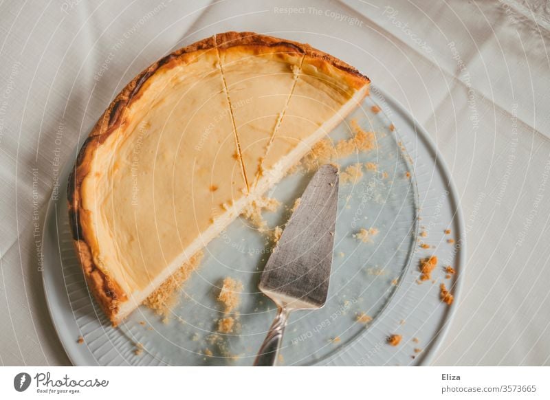 Ein halber Käsekuchen auf einer Servierplatte mit einem Kuchenheber Tisch lecker gelb Krümel süß Tischdecke weiß Dessert Vogelperspektive backen Torte