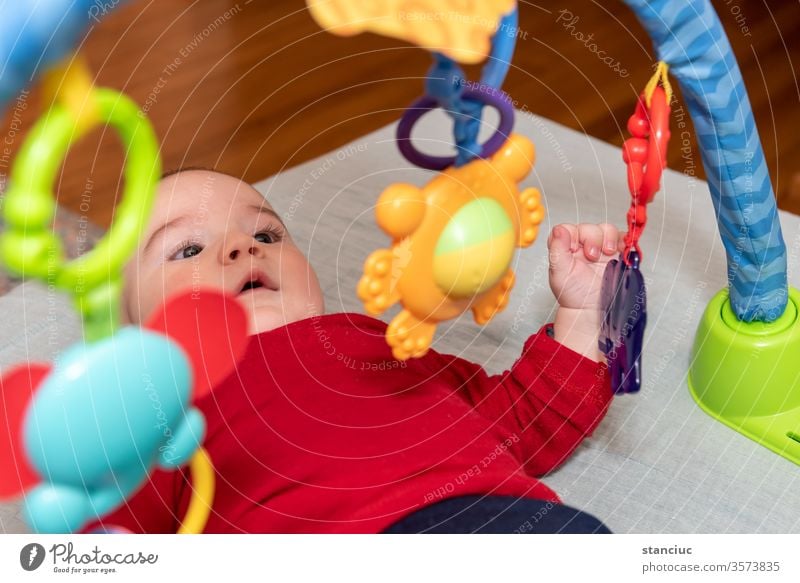 Bezaubernder 6 Monate alter kleiner Junge auf dem Rücken, umgeben von buntem Spielzeug Neugier spielen Genuss Kleinkind Baby niedlich Gesichtsausdruck 6-12
