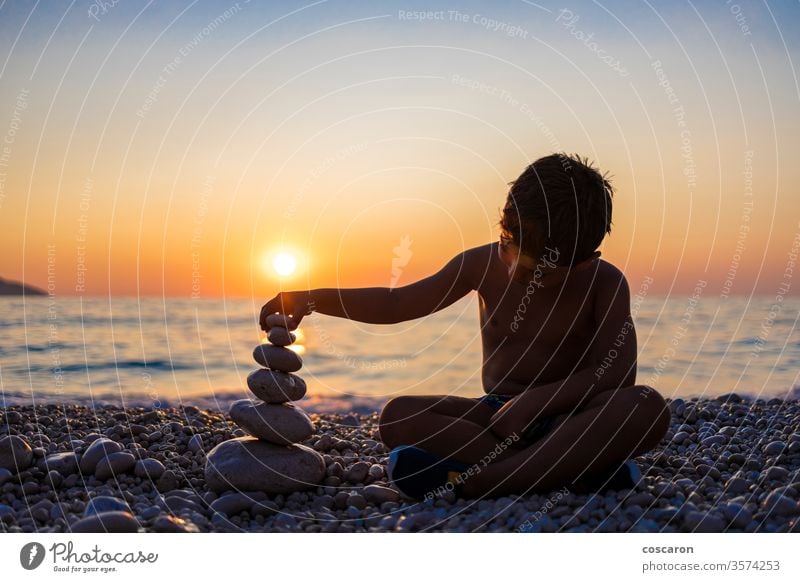 Kleines Kind spielt mit Steinen am Strand bei Sonnenuntergang Aktivität Hintergrund Gleichgewicht Ausgewogenheit schön Schönheit Junge Kindheit Textfreiraum