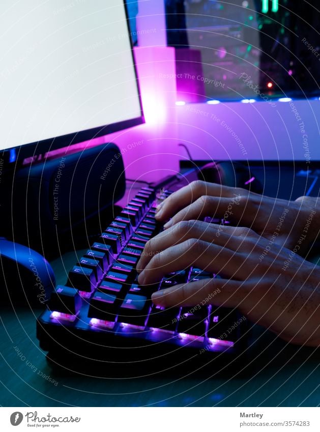 Bild von Männerhänden beim Tippen. Hände eines Spielers auf einer Tastatur. Der Hintergrund ist mit LED-Leuchten beleuchtet. Computer Keyboard Finger Schütze