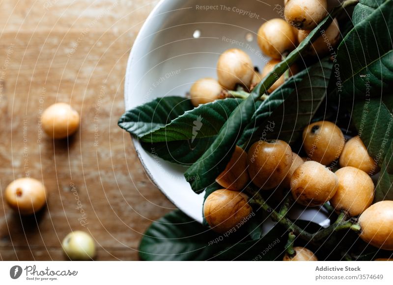 Frischer Zweig von Mispelfrüchten auf dem Tisch nispero loquat Ast gesunde Ernährung weiß Keramik Teller hölzern schäbig frisch grün Blatt Schreibtisch rustikal