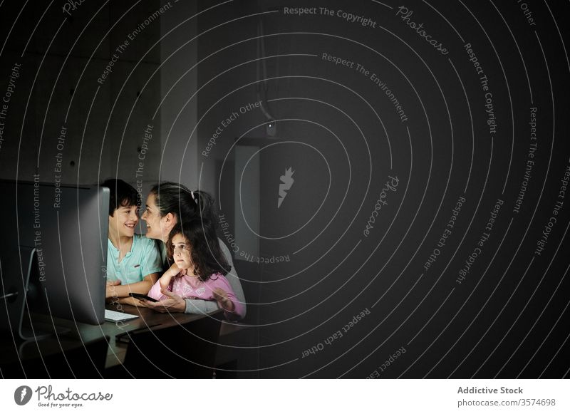 Fröhliche Frau mit Kindern schaut Video am Computer an Mutter benutzend Smartphone Zusammensein Telearbeit Kinderbetreuung Glück heiter heimwärts Kommunizieren