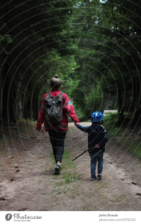 Frau läuft mit Kind spazieren im Wald Waldweg Erde Tannenzapfen Bäume Fichtenwald Fahrradhelm wandern laufen Dutt fleecejacke Regenjacke Chucks gemeinsam