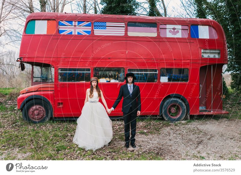 Neuvermähltes Paar in der Nähe des roten Busses im Wald Jungvermählter roter Bus Hochzeit elegant Doppeldeckerbus Braut striegeln Händchenhalten Liebe Kleid