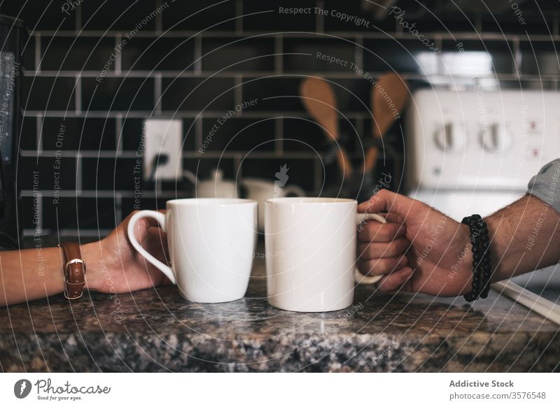 Unerkanntes Paar, das in der Küche Tassen mit heißem Getränk trinkt Hand nehmen trinken Zusammensein Partnerschaft Tisch Murmel Armbanduhr Keramik Wand Freund