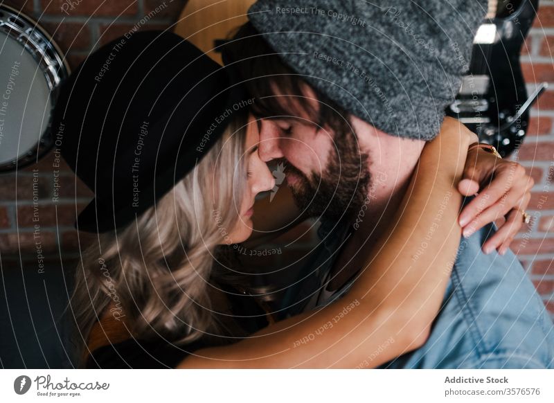 Paar umarmt sich auf dem Sofa in der Wohnung Umarmen Kuss Hipster Loft Partnerschaft Liebe Innenbereich Musiker Freund Zuneigung Zusammensein Augen geschlossen