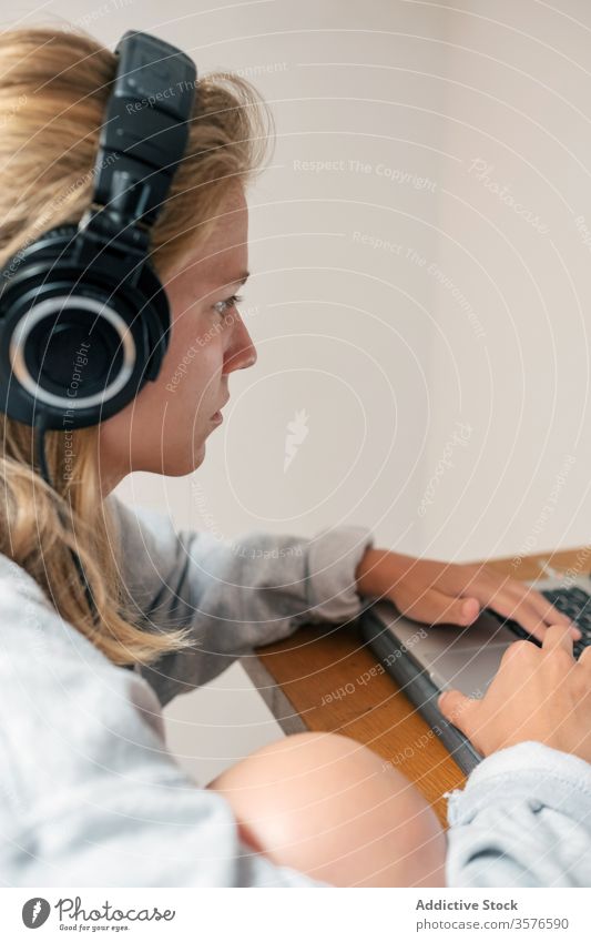 Junge Frau mit Kopfhörern am Laptop benutzend heimwärts Spieler lässig jung Browsen zuhören Apparatur ernst Fokus Gerät spielen Computer Lifestyle Internet