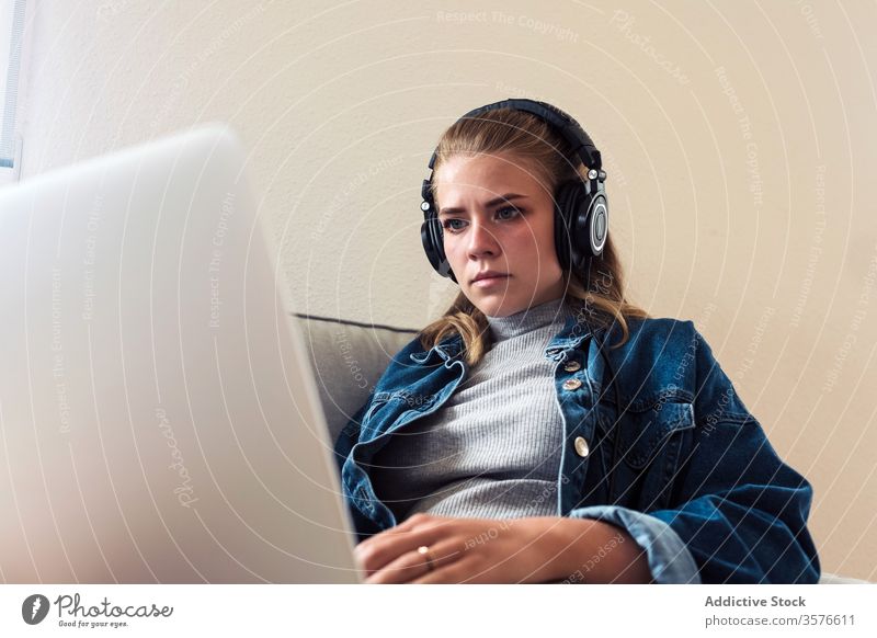 Moderne Frau, die zu Hause mit dem Laptop arbeitet heimwärts Kopfhörer Sofa benutzend Fokus Konzentration Arbeit jung lässig Drahtlos abgelegen Projekt