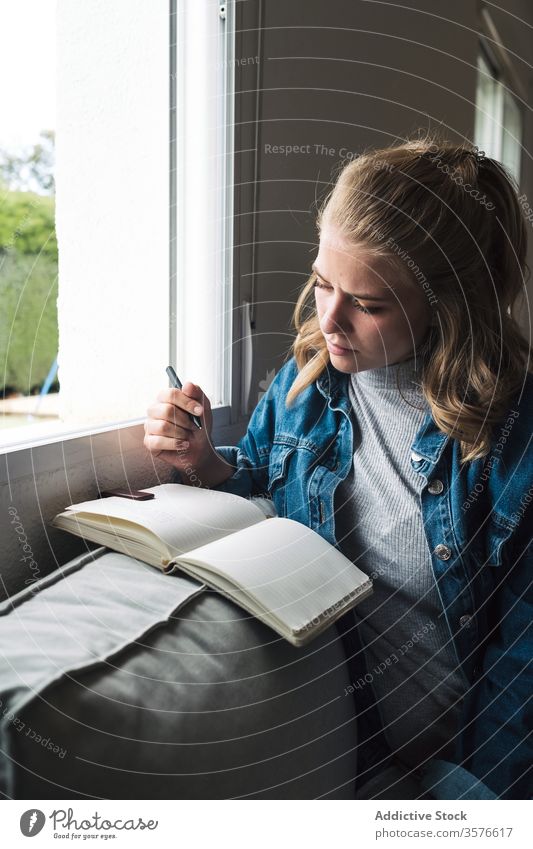Nachdenkliche Frau mit Notebook am Fenster sitzend Tagebuch heimwärts besinnlich jung Schüler Notizblock nachdenklich lesen lässig Denken Windstille ruhig
