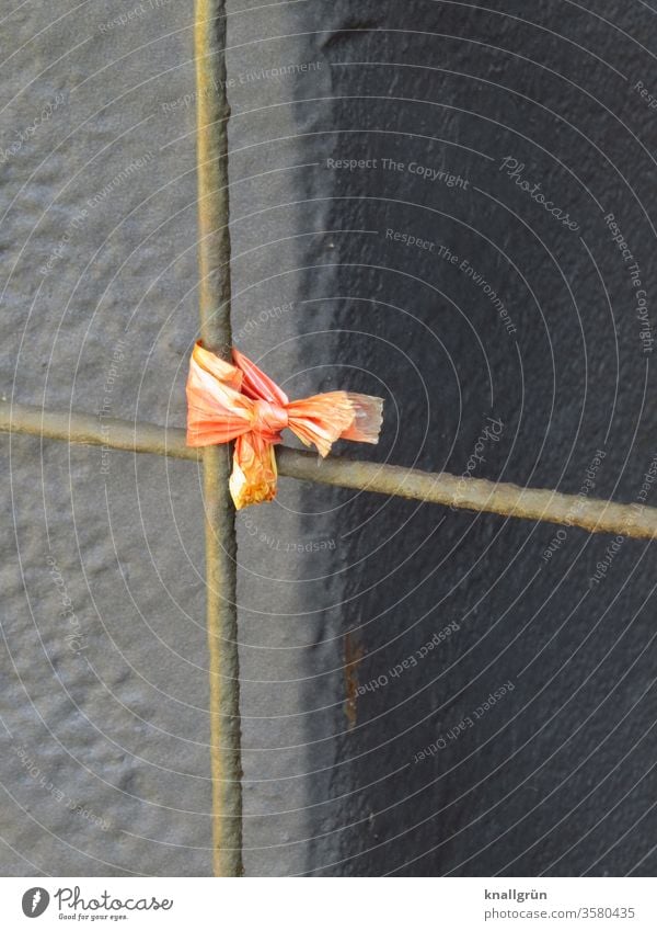 Verknoteter Rest eines orange Flatterbandes an einer rostigen Eisenstange eines Zaunes vor braunem Hintergrund Knoten Sicherheit verknotet Eisenstangen