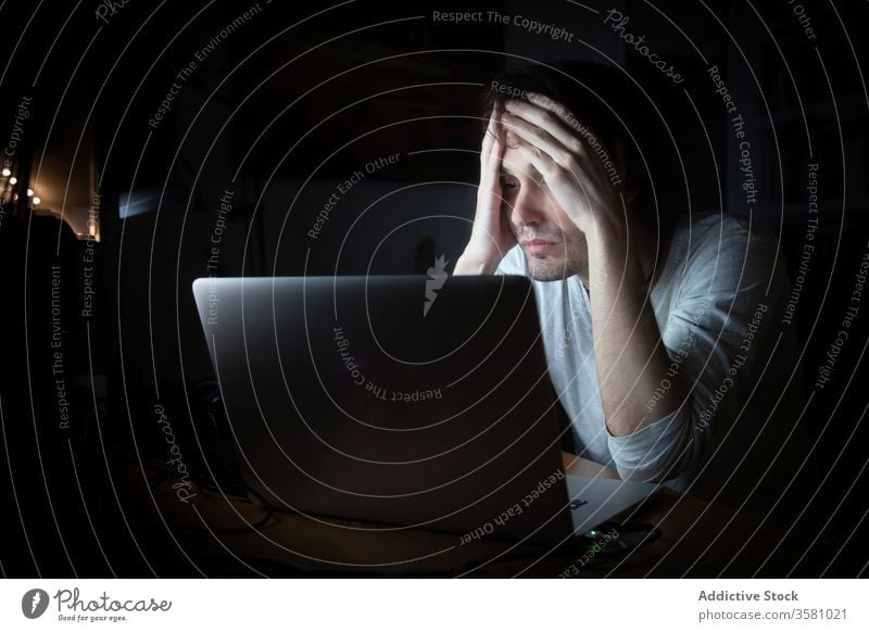 Müder Mann, der nachts mit dem Laptop arbeitet Arbeit heimwärts Nacht müde erschöpft online abgelegen dunkel Quarantäne Stress Telearbeit jung männlich lässig