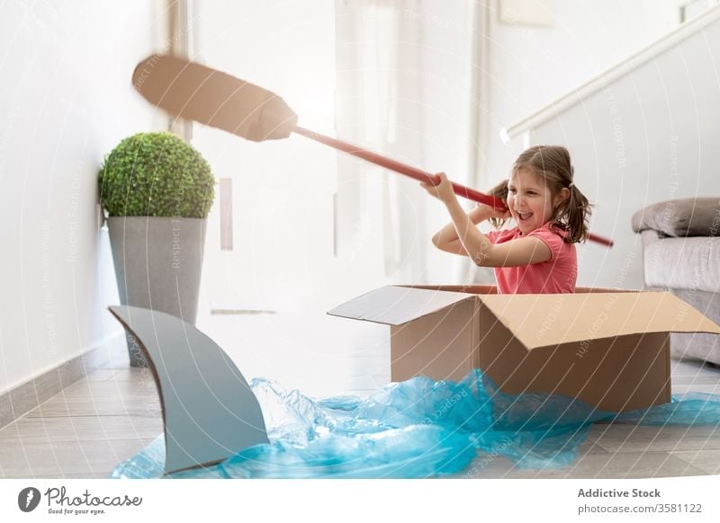 Fröhliches kleines Mädchen in Pappkarton segelt vom Hai weg Haifisch Boot Paddel Spiel Vorstellungskraft Spaß spielerisch Kind Kasten spielen Matrosen heimwärts