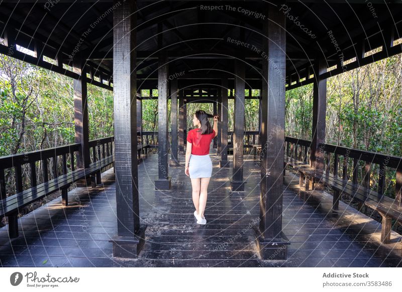 Asiatin auf Holzveranda im Wald bei Tageslicht stehend Frau Veranda Bank Spalte Architektur Haare berühren Freizeit Erholung Antiquität Gelassenheit hölzern