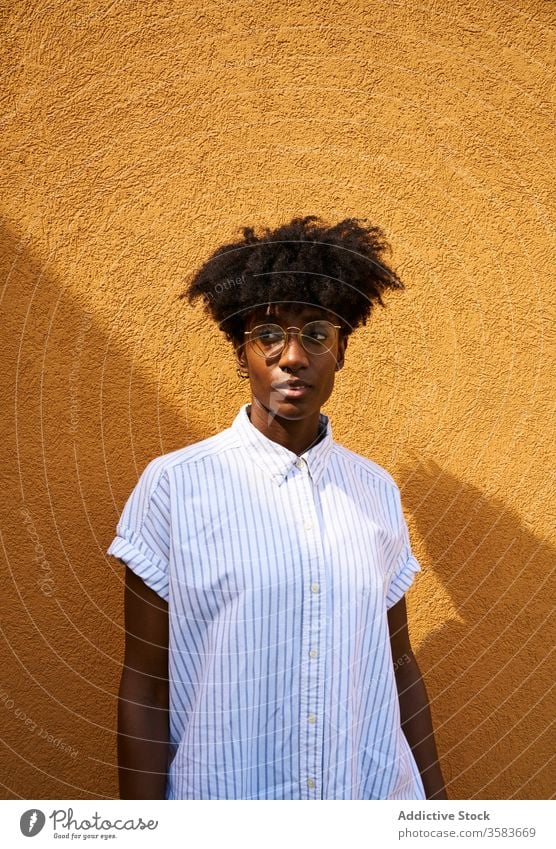 Stilvolle, nachdenkliche schwarze Frau an einem sonnigen Tag auf der Straße Persönlichkeit trendy farbenfroh Afro-Look ruhig besinnlich Brille Windstille