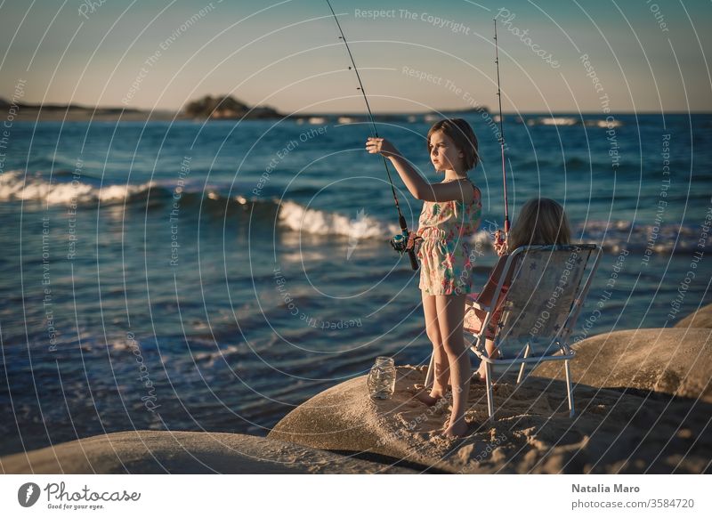 Zwei kleine Mädchen fischen bei Sonnenuntergang in der Brandung des Ozeans. Sommerfreizeit, Hobby und Spaß für Kinder. Fischen Freizeit Menschen Urlaub Person