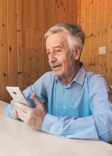 Glücklicher grauhaariger älterer Mann, der ein Smartphone benutzt und während des Coronavirus einen Videoanruf bei seinen Enkelkindern oder seiner Familie zu Hause tätigt. Er schaut sich lustige Videos in sozialen Netzwerken an.