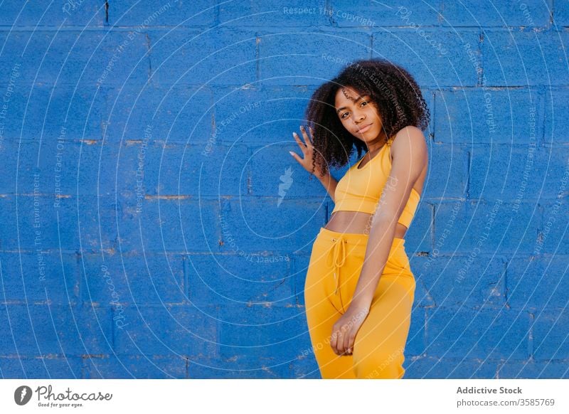 Ruhige ethnische Frau mit ausgestreckten Armen nahe der blauen Wand Afro-Look Frisur ausdehnen ruhig lebhaft pulsierend hell Dehnung schwarz Afroamerikaner