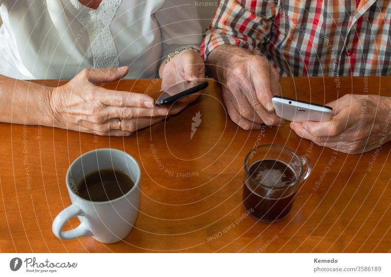 Draufsicht auf alte Menschen, die zu Hause Smartphones benutzen, während sie Tassen mit heißen Getränken genießen. Konzept von älteren Menschen und Technik.