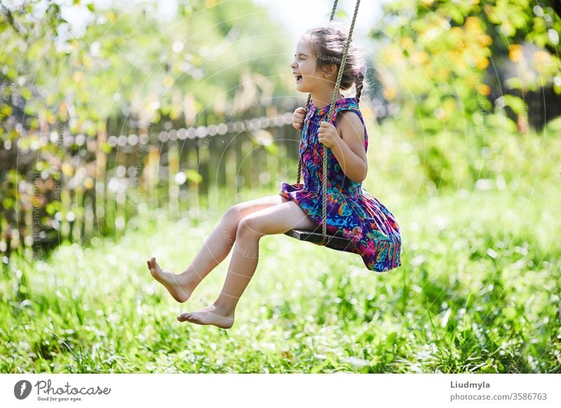Ein glückliches kleines Mädchen lächelt und schaukelt an einem sonnigen Sommertag im Garten. Lachen lustig pendeln im Freien swinging Lächeln Sommerzeit