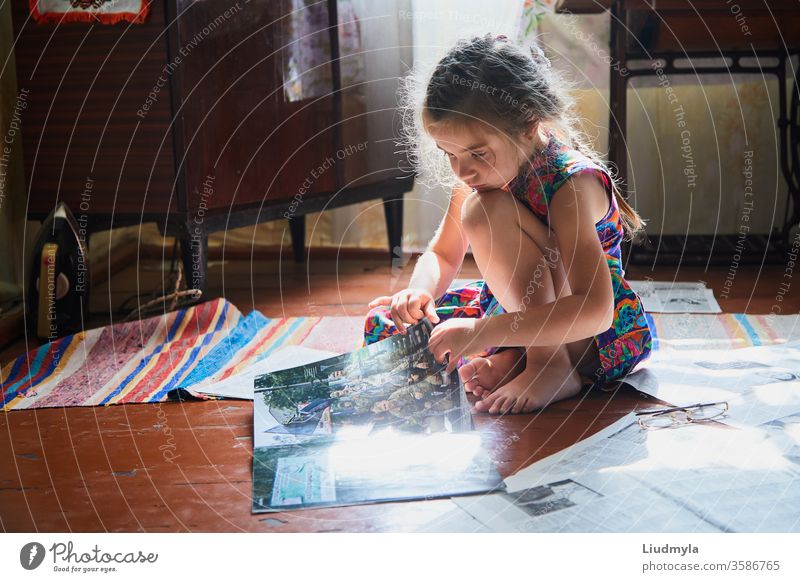 Ein kleines Mädchen sitzt und schaut in ein Magazin auf dem Boden im Haus. lesen Zeitung Sitzen Neugier Kinder Lifestyle Zeitgenosse Erfahrung Wissen elementar