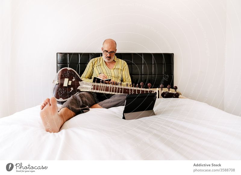 Älterer männlicher Musiker, der zu Hause Sitar spielt sitar Mann spielen Tablette benutzend online Lektion älter Notebook zur Kenntnis nehmen Apparatur Gerät