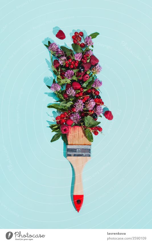Borstenmalpinsel mit verschiedenen Beeren, Blumen und Blättern auf pastellblauem Hintergrund Diät Ernte frisch Blüte Blumenstrauß Bürste Haufen Klee Konzept