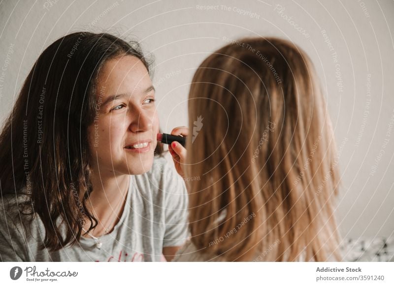 Bezaubernde Schwestern mit bemalten Gesichtern zu Hause Farbe Zeitvertreib heimwärts Mädchen Geschwisterkind Spaß haben Zusammensein spielerisch Partnerschaft