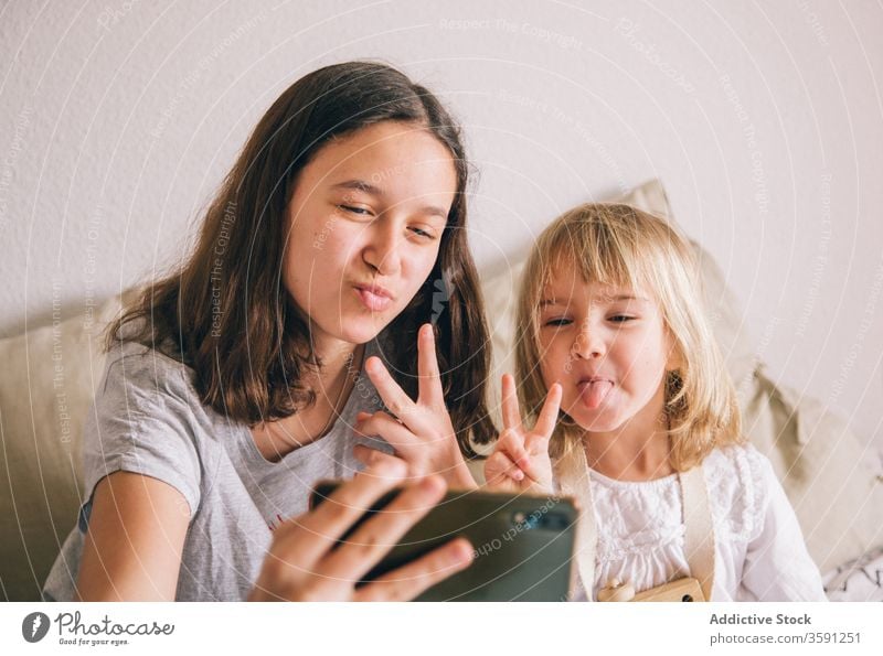 Fröhliche Schwestern, die sich zu Hause am Smartphone vergnügen Selfie Grimasse Mädchen Geschwisterkind benutzend v-Zeichen Spaß haben gestikulieren Teenager