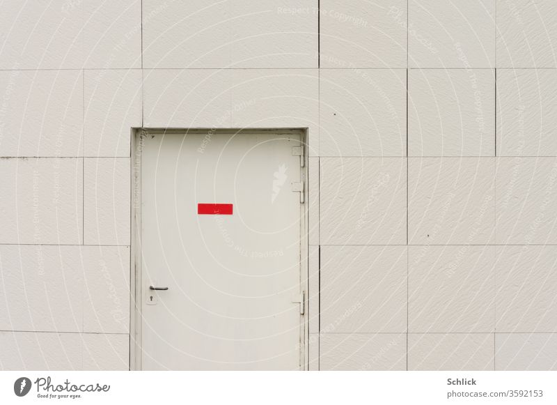 Graue Tür mit rotem Schild ohne Text in grauer Fassade eines Industriegebäudes Türschild leer Fassadenplatten Detail Textfreiraum Mitte Türgriff Scharniere zu