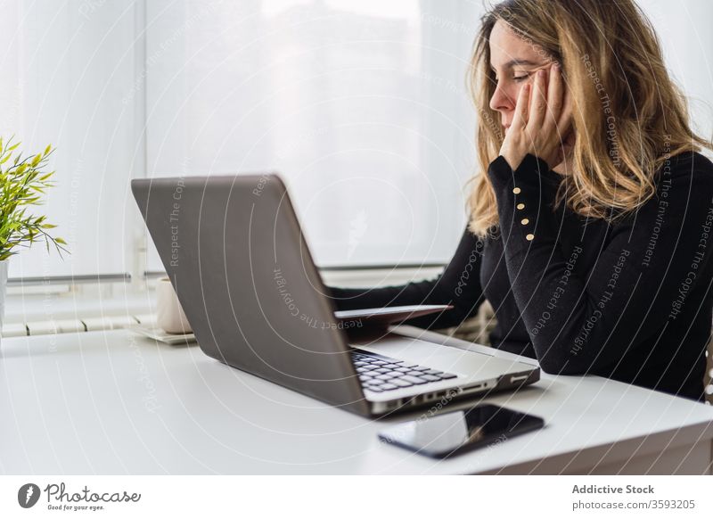 Junge Frau, die zu Hause mit dem Laptop arbeitet Arbeit heimwärts zur Kenntnis nehmen online abgelegen Tisch lässig beschäftigt jung Arbeitsplatz freiberuflich