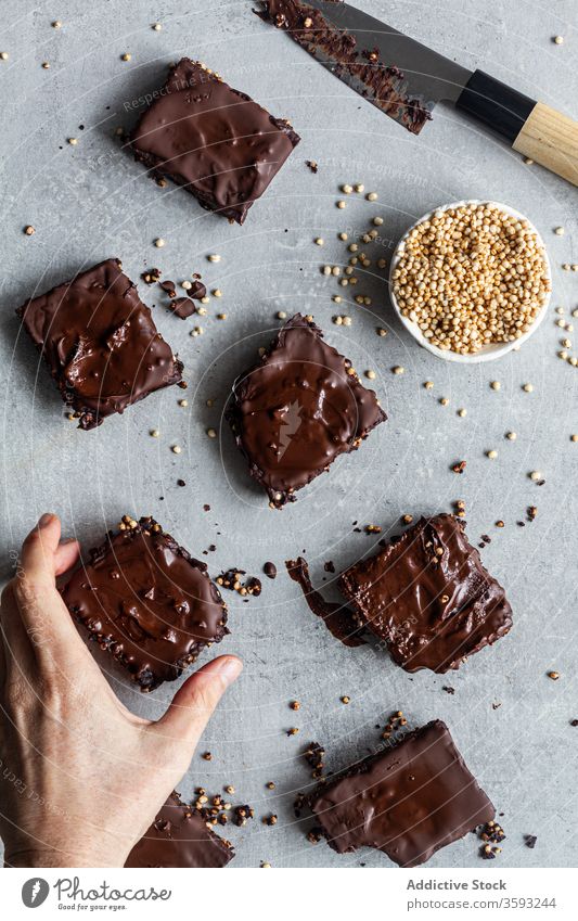 Anonyme Person, die mit Schokolade und Quinoa-Samen überzogene Brownies isst selbstgemacht lecker Bar Dessert Konditorei süß Pergament Messer dunkel Keks